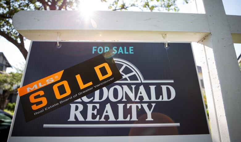 A 'SOLD' sticker obscures part of a realtor's 'For Sale' sign.