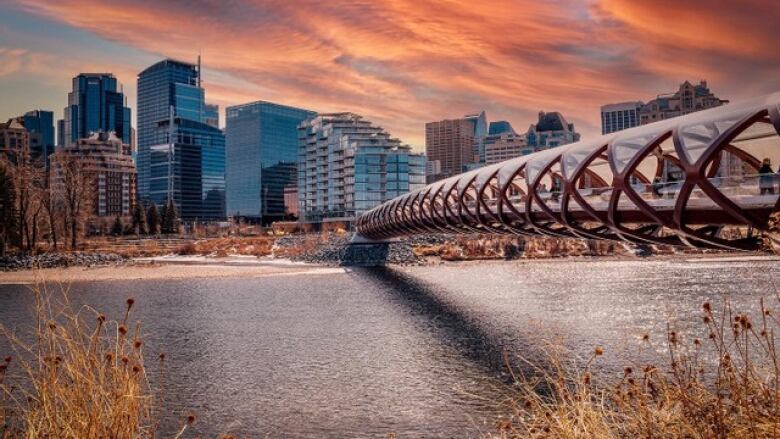 A straight-span red pedestrian bridge to downtown Calgary, as seen at sunset.