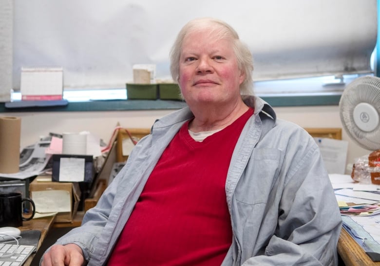 A man sits at a messy desk in an office.