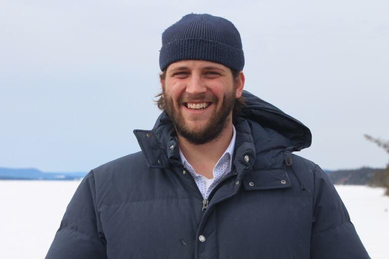 A man with a beard standing near an ice covered pond. 