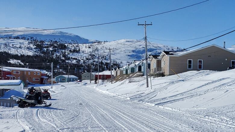 A snowy street with some houses on the right side and a mountain in the background.