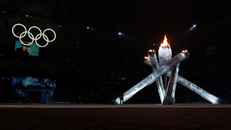 A large torch is seen burning with the Olympic rings in the background.