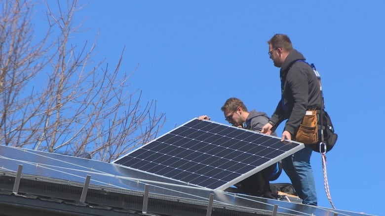 Two men install solar panels.