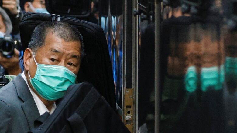 A older man in a grey suit, wearing a turquoise-coloured surgical mask, enters a building.