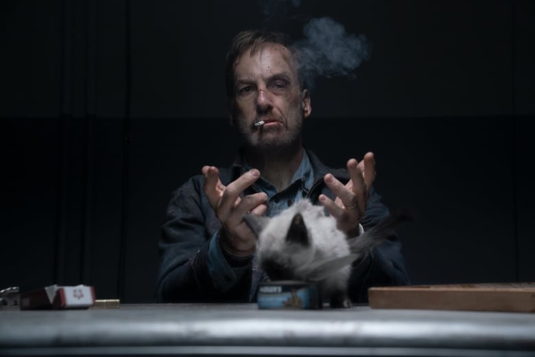 A still from a movie shows a badly beaten man with a cigarette dangling from his mouth as he sits in a dark room.