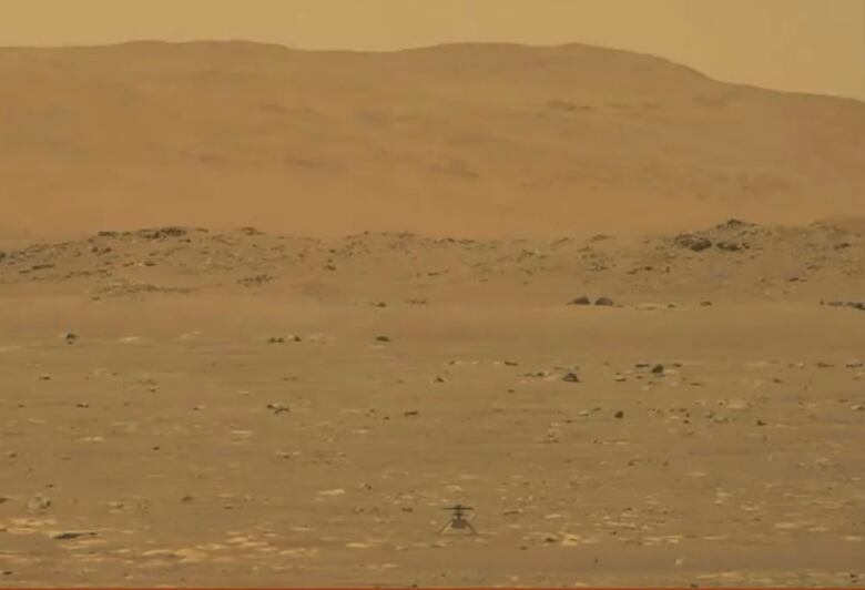 A tiny helicopter sits center frame, surrounded by dusty terrain.