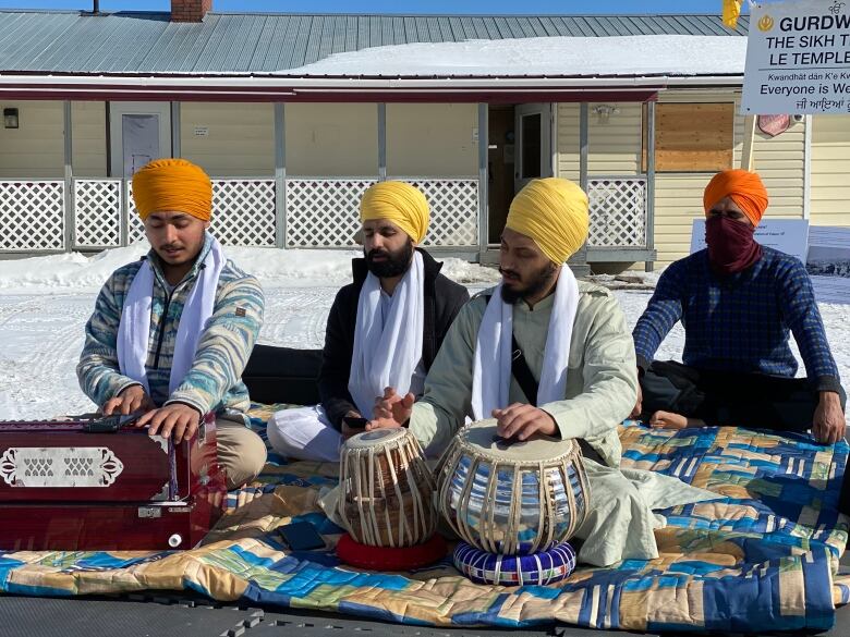 Four men sit on a bright blanket, playing music.