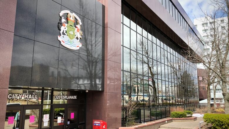 A building is shown made of large red and black stone blocks and tall mirrored windows with a crest and sign saying 