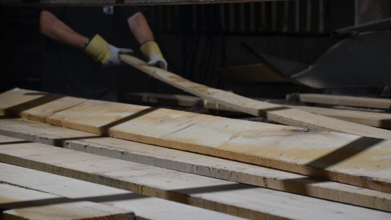 A worker grabs a wooden board off a pile of boards. 