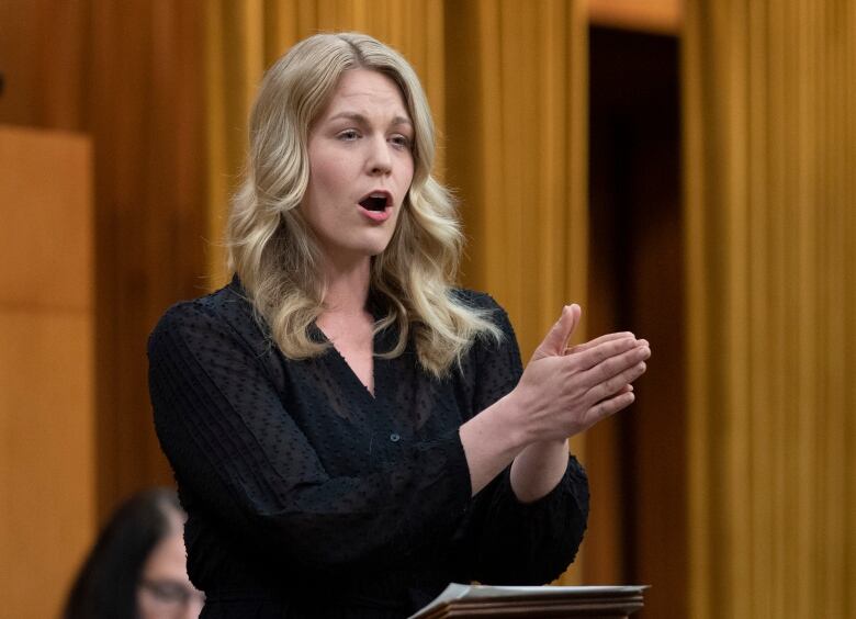 A woman in business wear gestures while speaking.