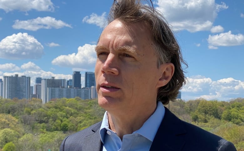 A man in a blazer and dress shirt standing outside with a skyline in the background