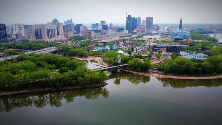 An aerial view of downtown Winnipeg, with The Forks and spring foliage in the foreground.