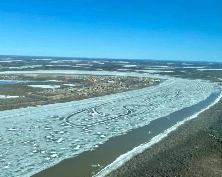 A small Arctic hamlet is seen from the air beside a partially ice-covered river.