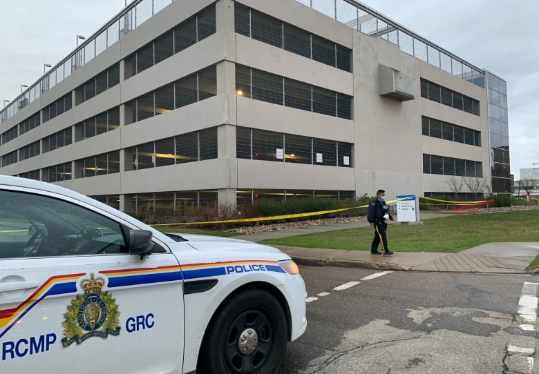 A RCMP car is parked in front of a 5-storey parkade on a summer day. 