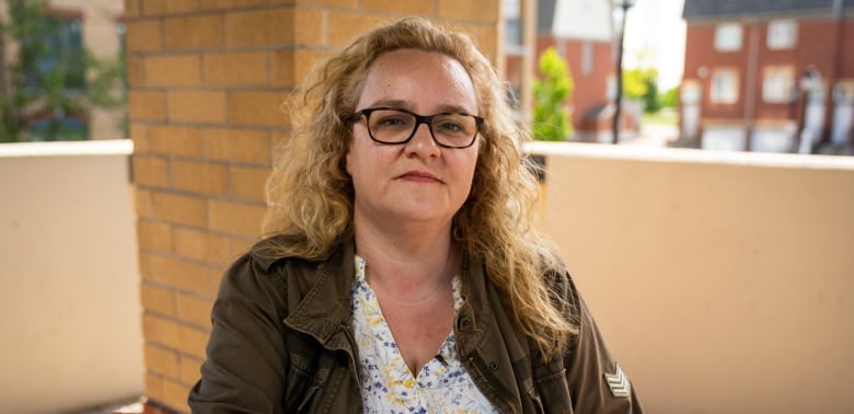 A woman sitting outside looks into the camera. 