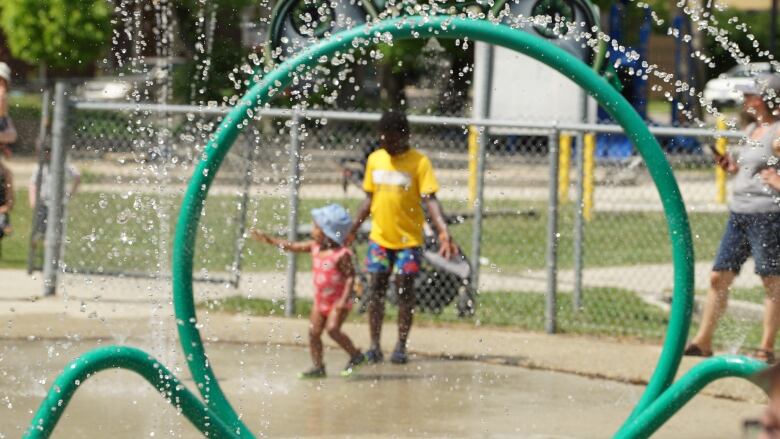 A green water park feature spraying water is shown in the foreground, with people in bathing suits blurred in the background.