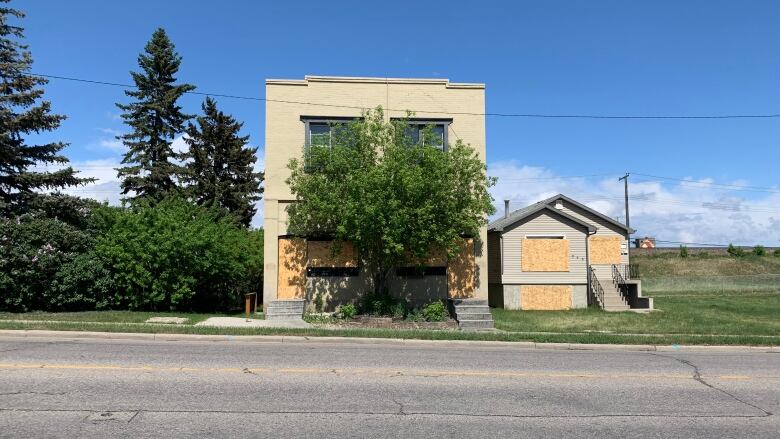 A boarded up building stands on the side of the road. 