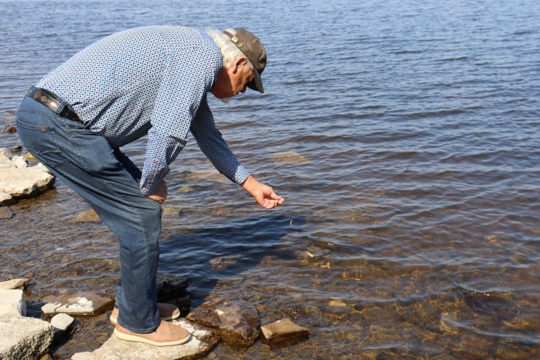 A man kneels to offer tobacco to a river with his left hand.