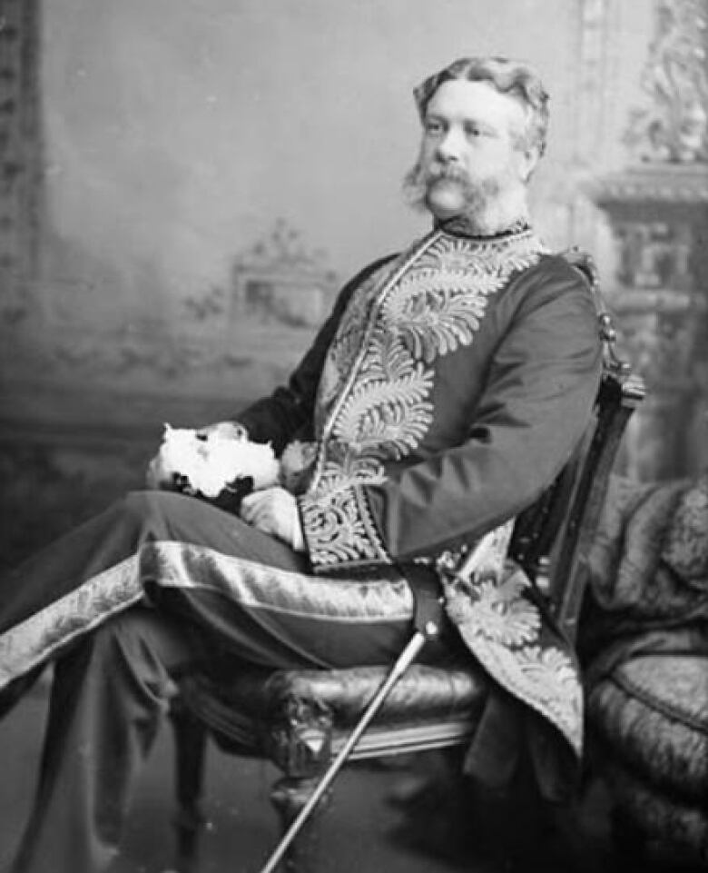 A black and white photo of a man seated in a chair. The man is wearing a livery coat and has a sword at his side.