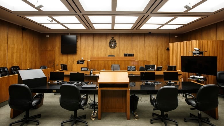 A wood paneled courtroom with black chairs in it. 