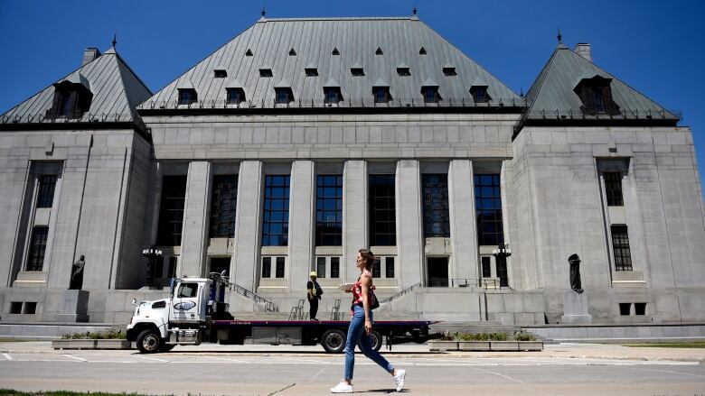 A woman walks in front of the Supreme Court of Canada on a sunny day