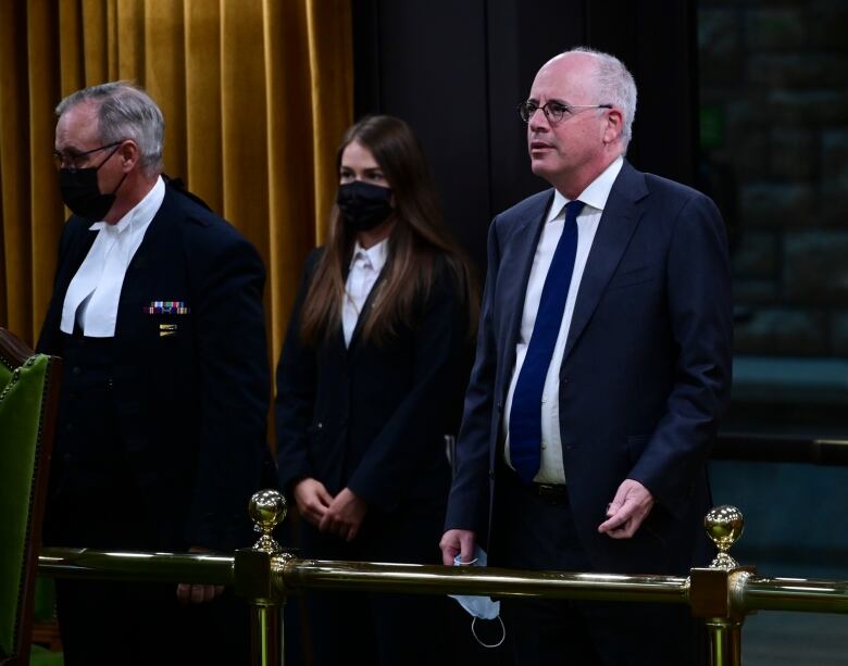 A man in a black suit and tie stands in the aisle of the House of Commons.