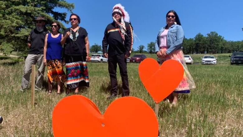 Indigenous leaders stand by large orange heart memorials.