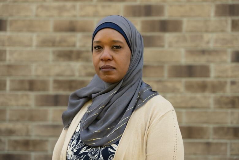 A woman in a hijab stands in front of a brick wall.