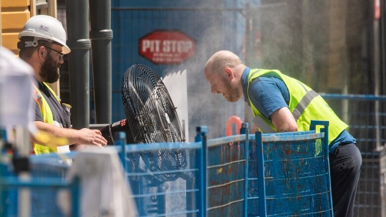 A construction worker uses a misting fan during a heat wave.