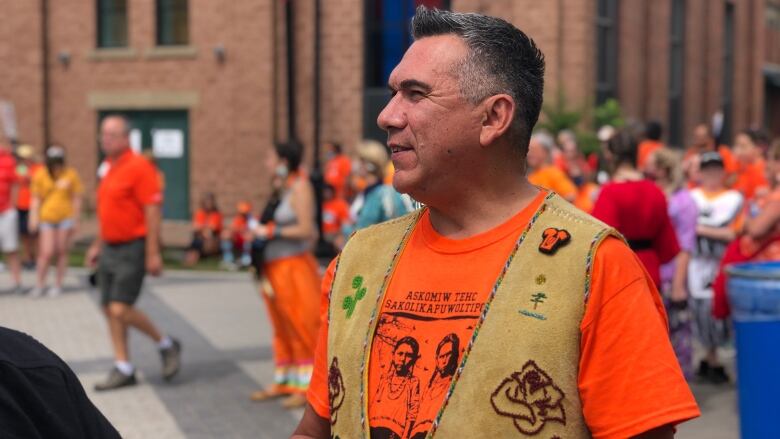 A man stands up outside wearing an orange shirt.