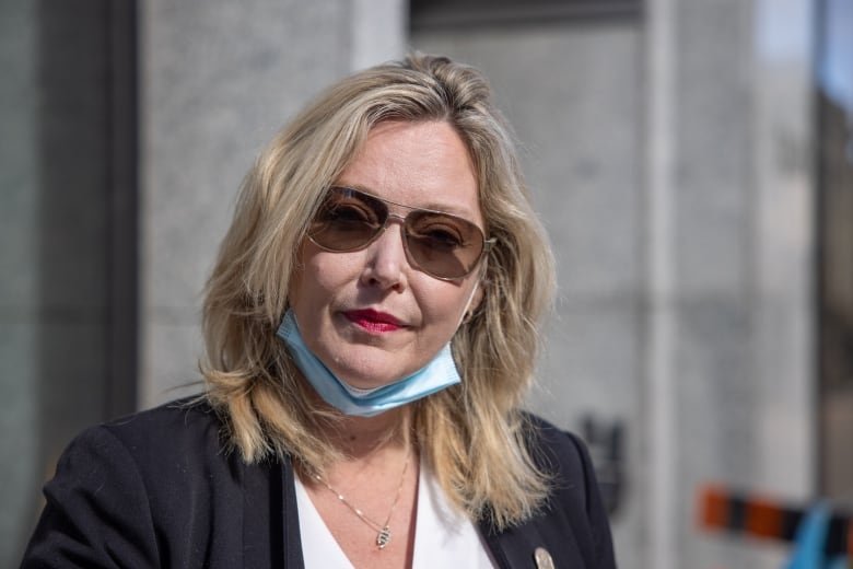 woman stands in front of building wearing sunglasses