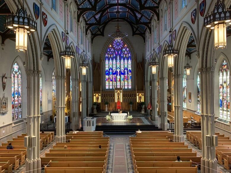 An interior photo of a cathedral shows tall arches, stained glass windows and church pews.