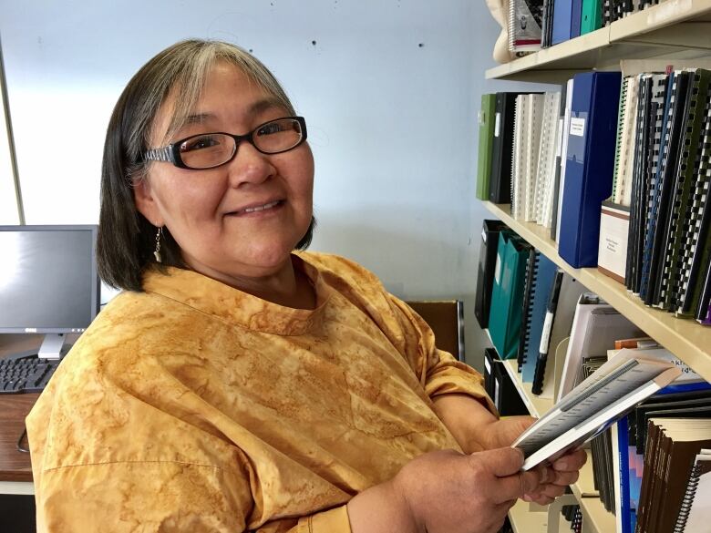 A woman stands holding a book in a library.