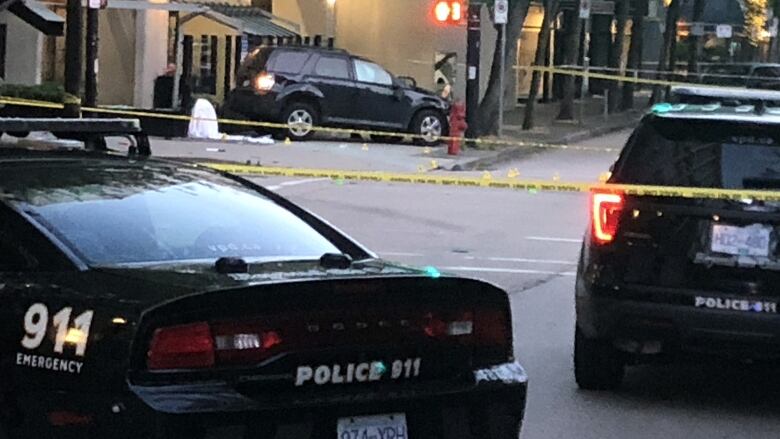 Two Vancouver police cars are in the foreground, with yellow police tape strung across the photo in multiple places. In the background a black SUV is seen on the sidewalk. It appears to show an airbag deployed inside the passenger window.