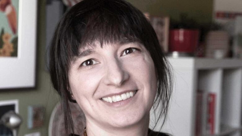 A woman smiles at camera, in the background there are bookshelves