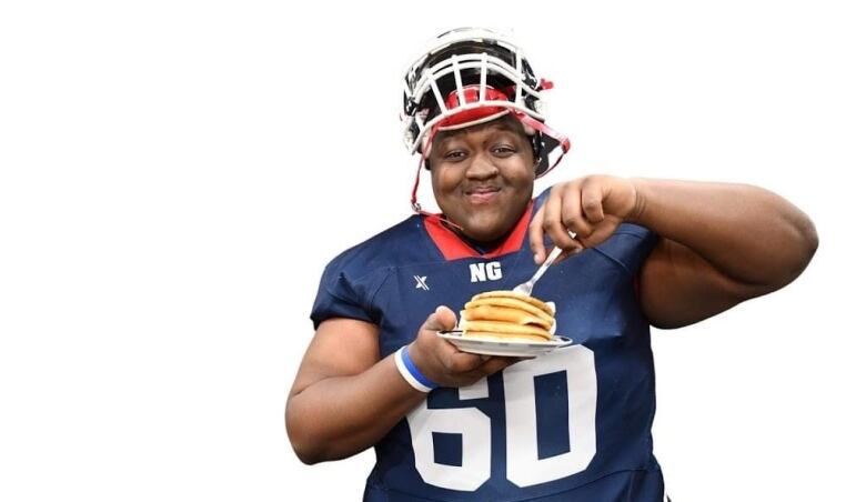 A boy in a football jersey holds up a plate of pancakes.