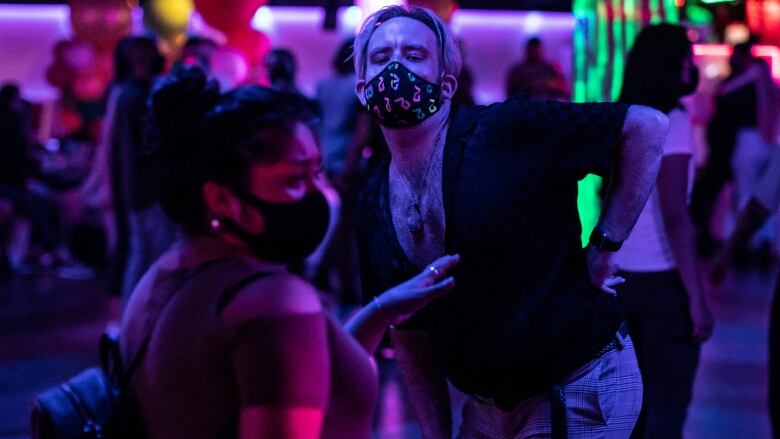 A group of young people dance in a club with purple and pink neon lighting.