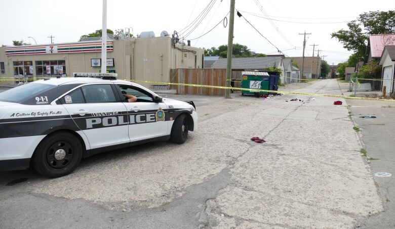 A police cruiser near a crime scene behind a 7-Eleven store.