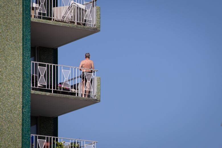 A shirtless man stands on his balcony in Vancouver.