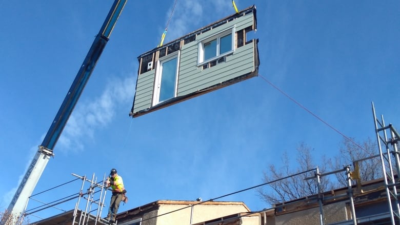 A crane carrying a panel of a house in the air. 