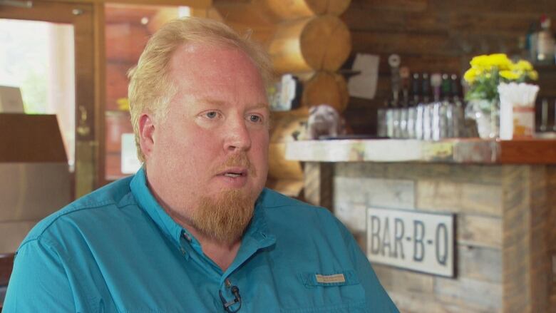 A man with blonde hair and a french beard speaks to a camera.