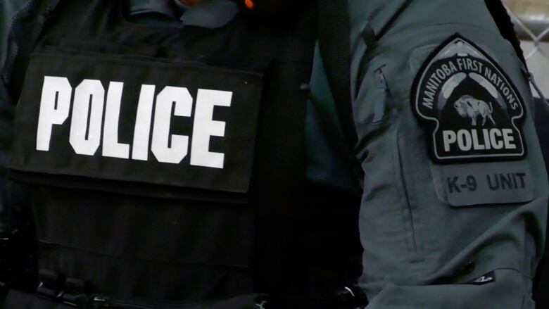 A close up of a person's torso. They are wearing a black vest that says police on it, and a dark grey jacket. On the sleeve of the jacket's arm is a patch that says Manitoba First Nations Police, K-9 unit.