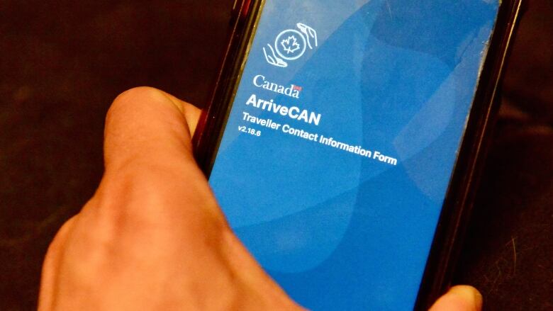 A close up shot of someone's hand holding a phone with the screen opened to the ArriveCAN app.