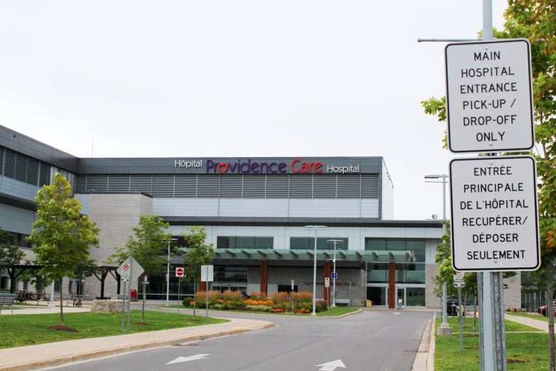 A hospital building round-about with signs indicating where to drive. There is a logo on the side of the building which reads 