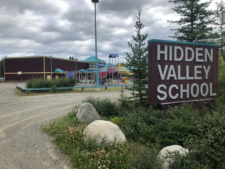 A school building is seen from the outside, with a sign reading 'Hidden Valley School.'