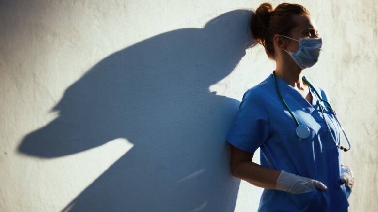 A nurse is pictured leaning against a wall, the light casting her shadow on the wall. 