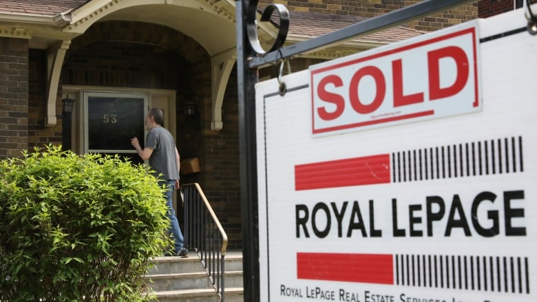 A man knocks on a door while a sold sign hands outside.