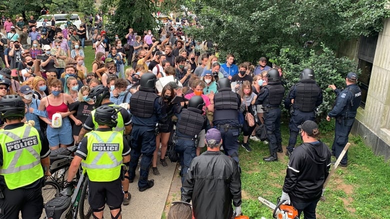 A large crowd of people is seen crushed together with linked arms facing police in uniform standing or beside bicycles