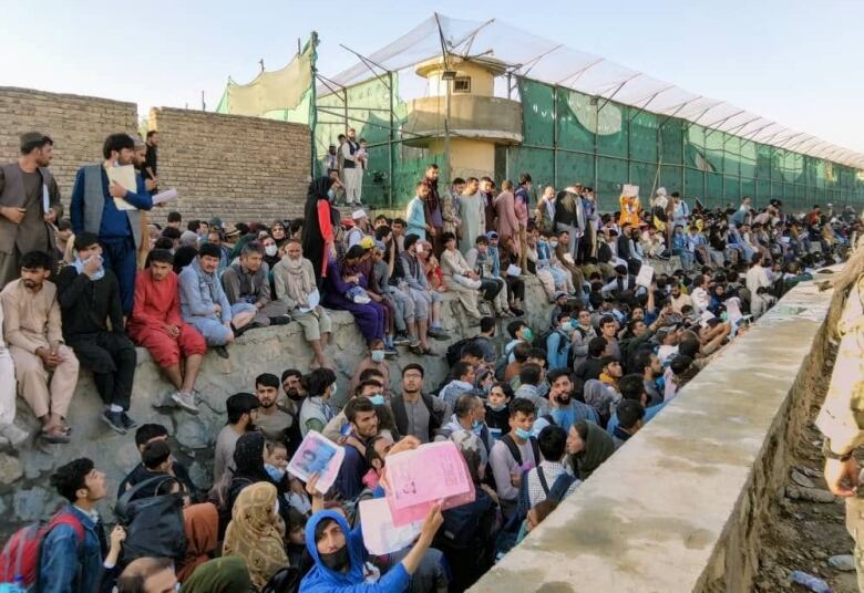 People sit on walls, crowded together, on an airfield.