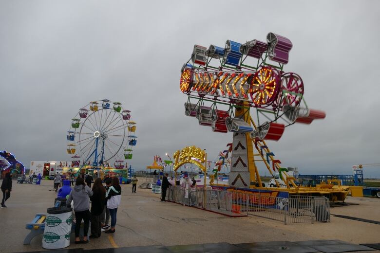 Fair rides, including a ferris wheel, are pictured outside under a dark and cloudy sky.